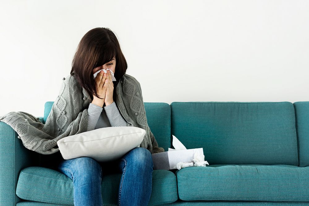 Sick woman sneezing on the sofa
