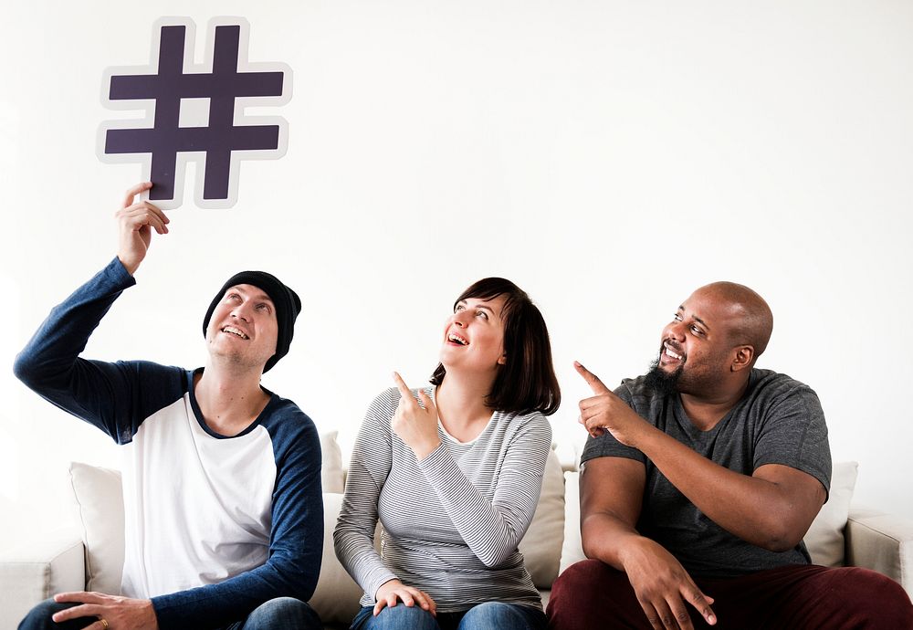 Group of diverse friends sitting on couch holding a hashtag icon