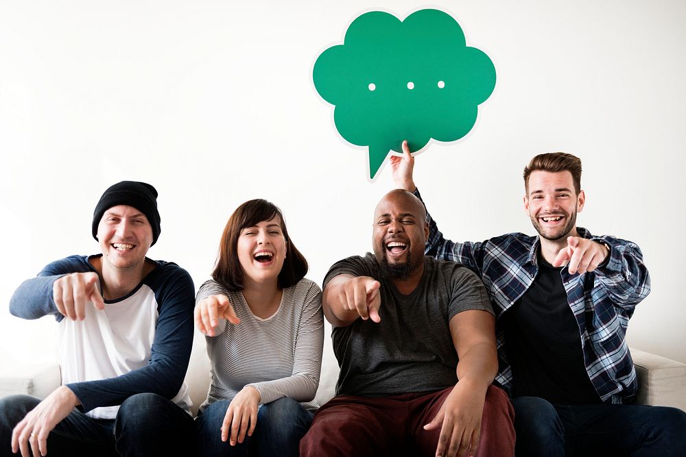 Group of diverse friends laughing pointing finger at the camera holding a speech bubble icon
