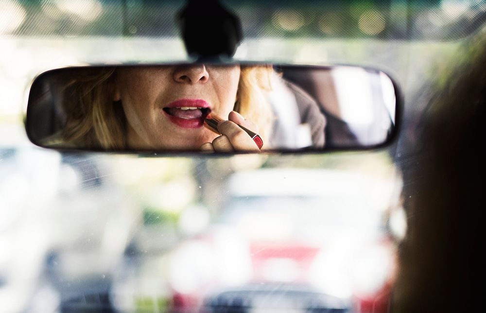 Woman putting on lipstick in a car