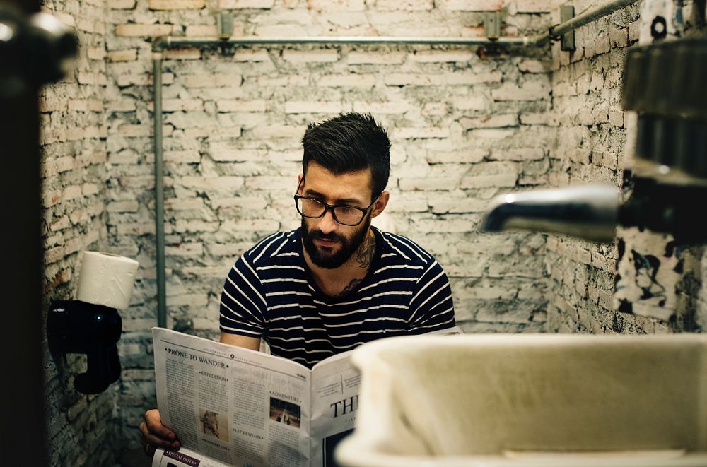 Man in a restroom reading newspaper