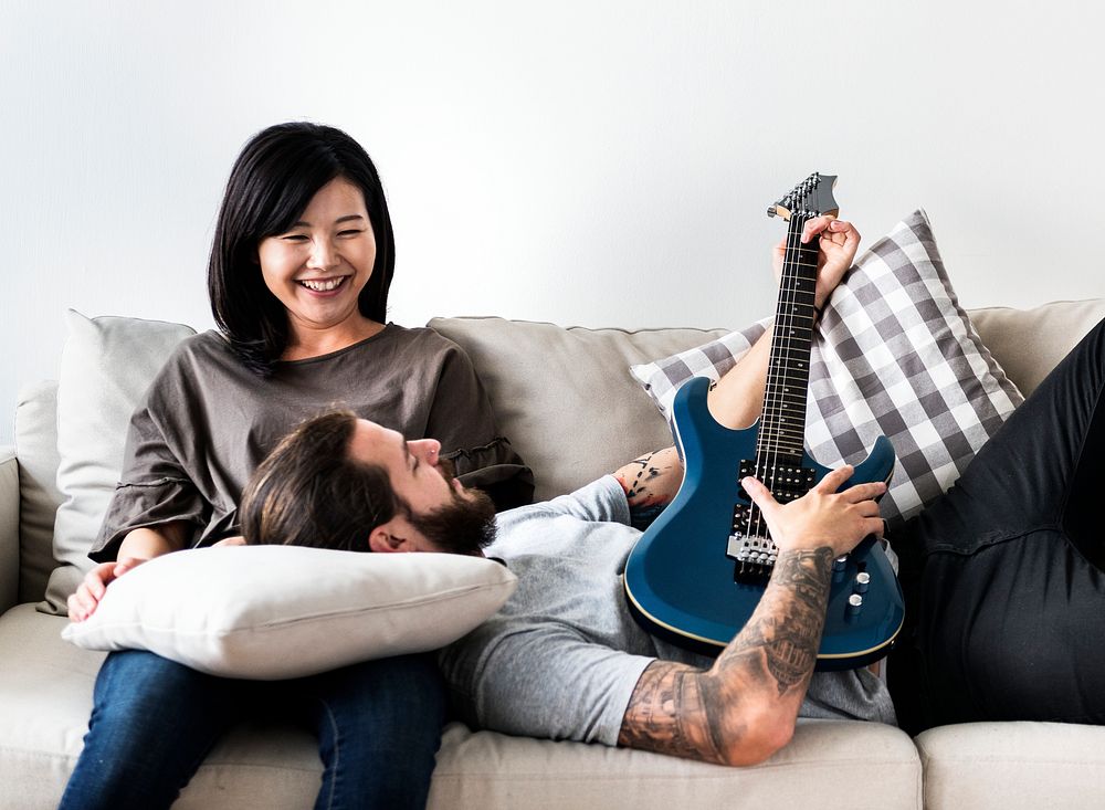 Cute couple on a couch boyfriend playing a guitar music and love concept