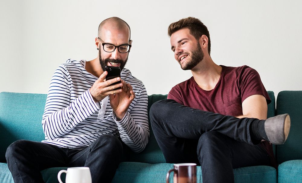 Two men on couch chilling and playing with mobile