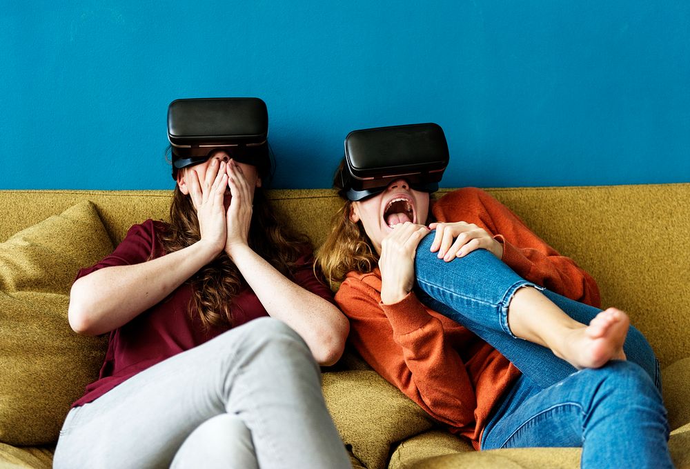 Two caucasian woman using VR on a sofa