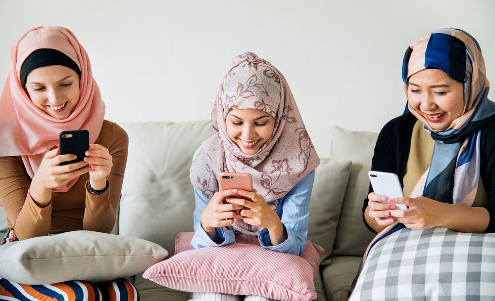 Group of islamic girls sitting on the couch and using smart phones