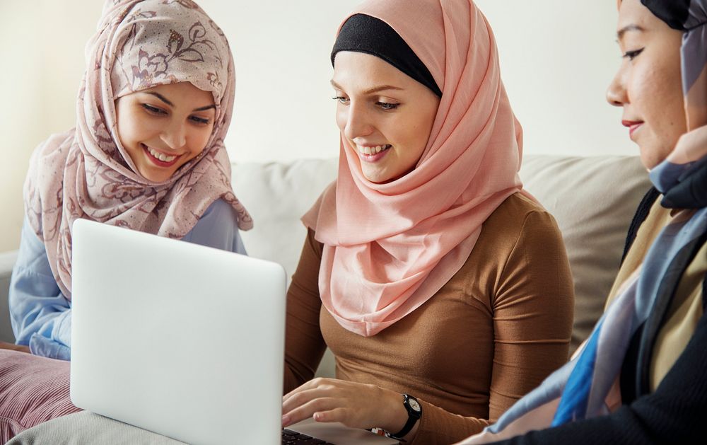Islamic women friends sitting on the couch talking and using laptop