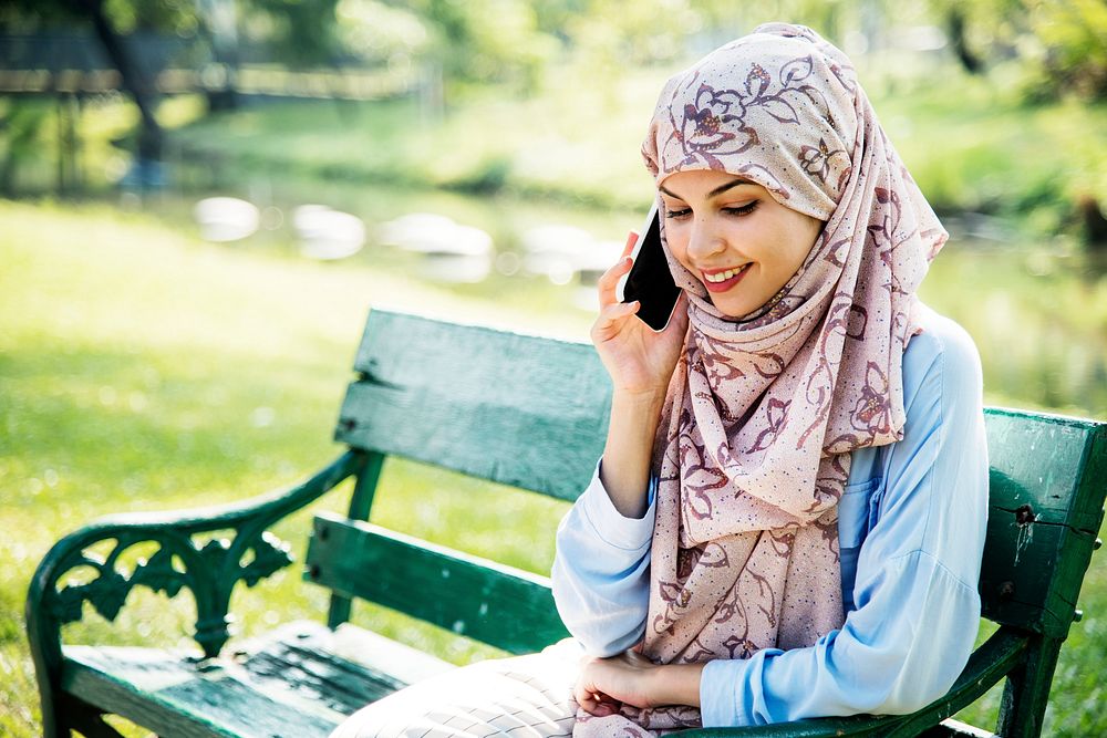 Islamic woman using mobile phone with smiling at park
