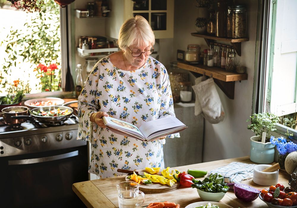 Elderly woman reading a cookbook in the kitchen