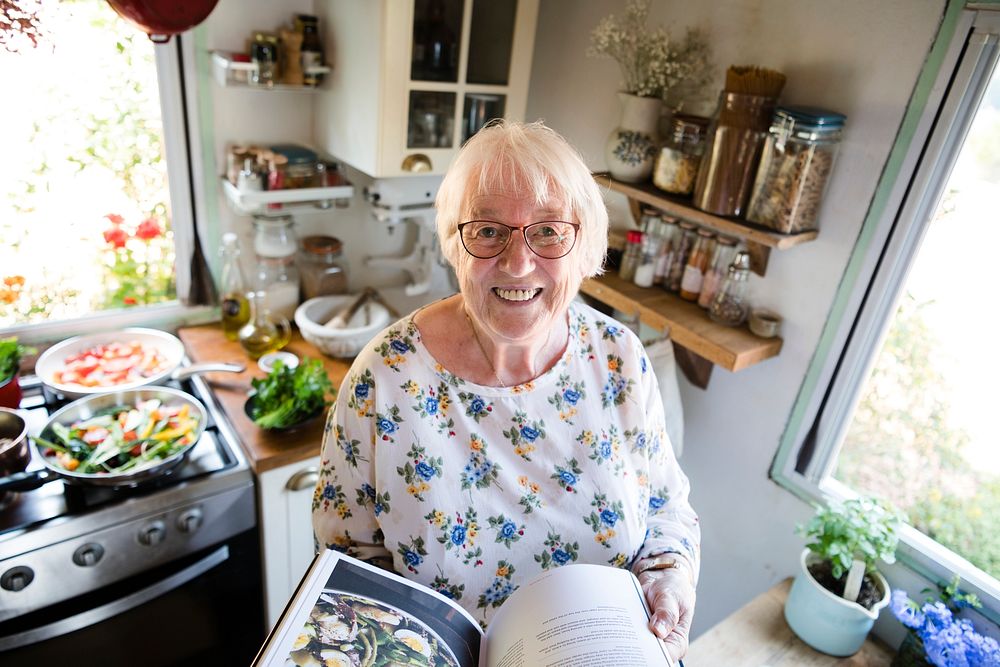 Happy elderly woman reading a cookbook | Photo - rawpixel