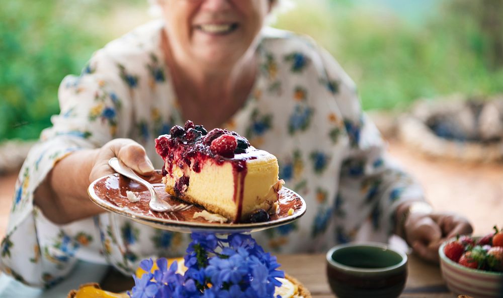 Grandmother holding a slice of cheesecake with mixed berries sauce