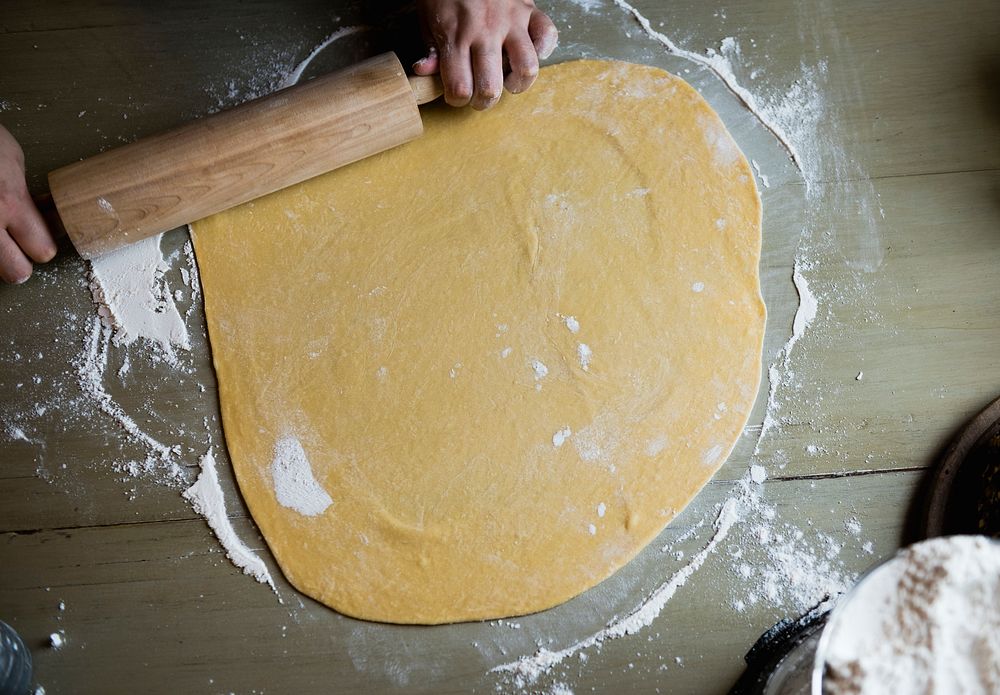 Hands rolling out dough with a rolling pin