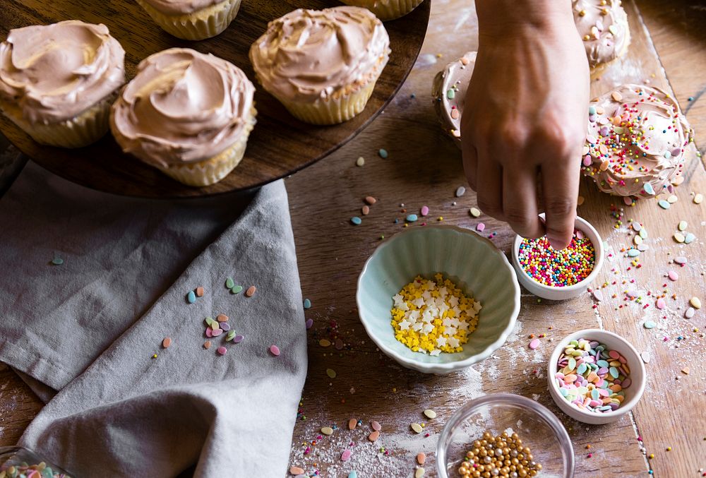 Hand adding sprinkles to chocolate cupcake food photography recipe idea