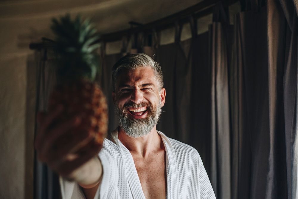 Man in a bathrobe holding a pineapple