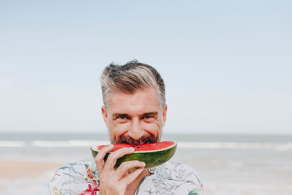 Mature man eating watermelon at the beach