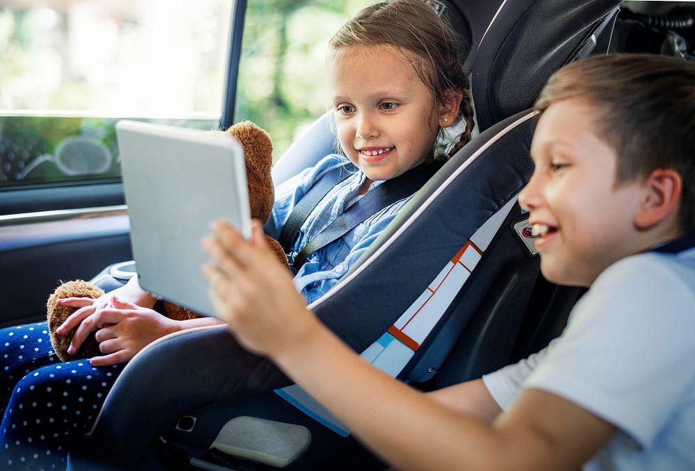 Sister and brother playing with digital devices in the car