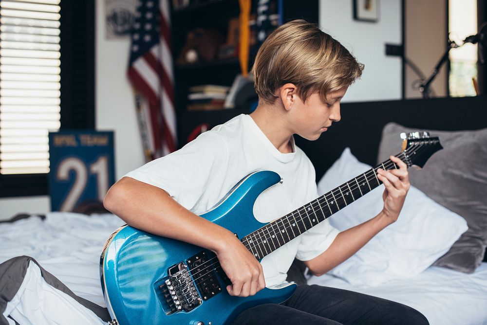 Young boy playing electrical guitar in his bedroom