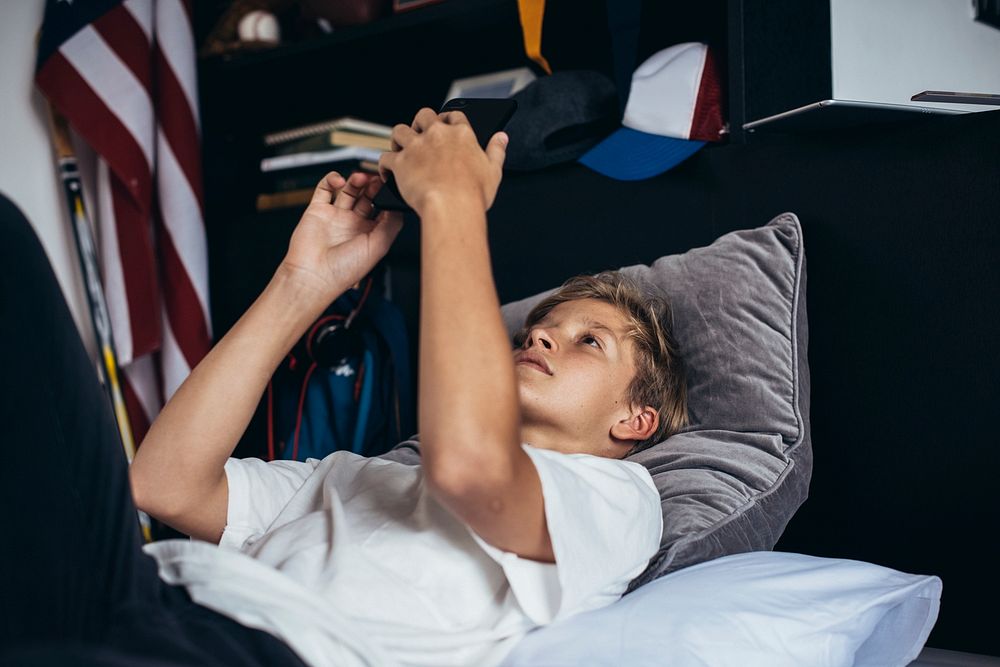 Young boy in bed playing on his phone