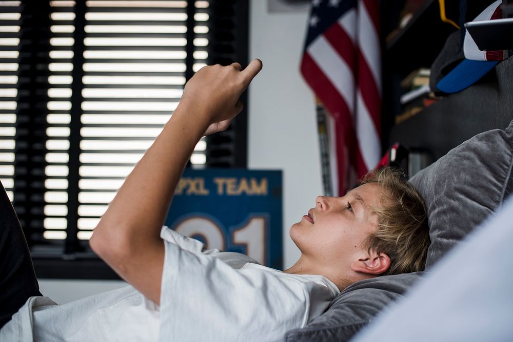 Young boy in bed playing on his phone