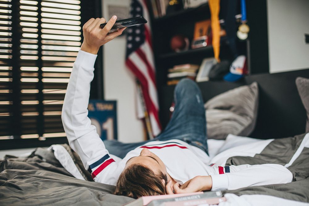 Teen lying in bed and watching videos on his mobile phone