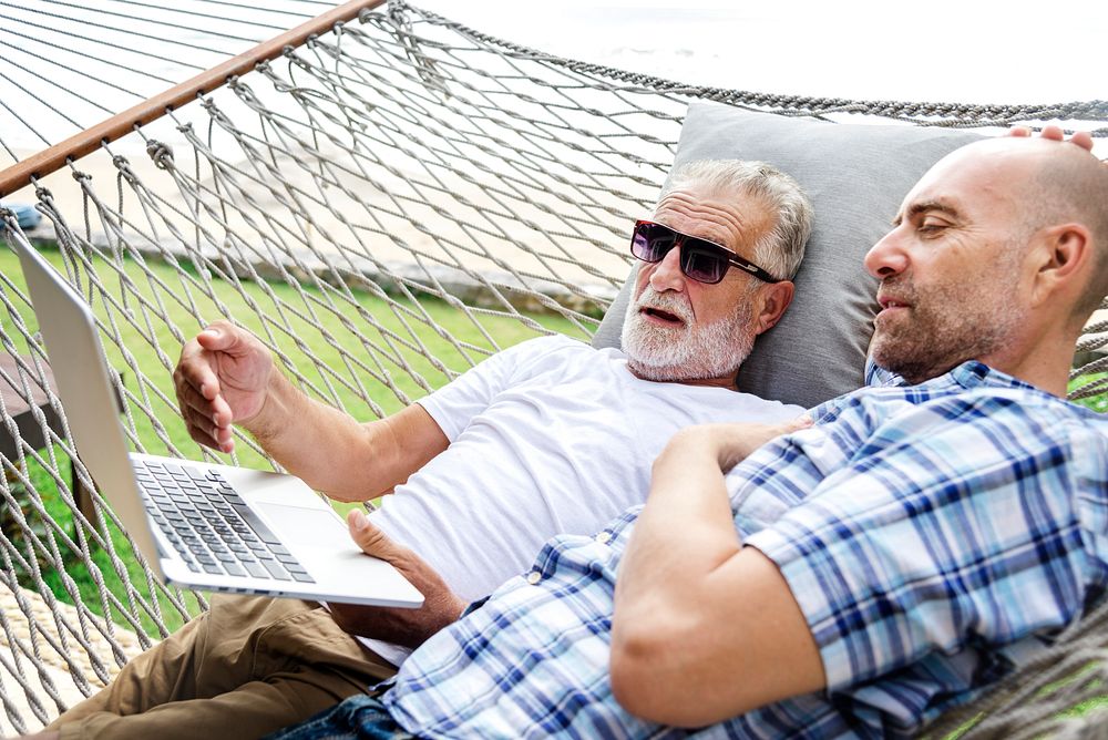 Senior men lying on a hammock using a laptop