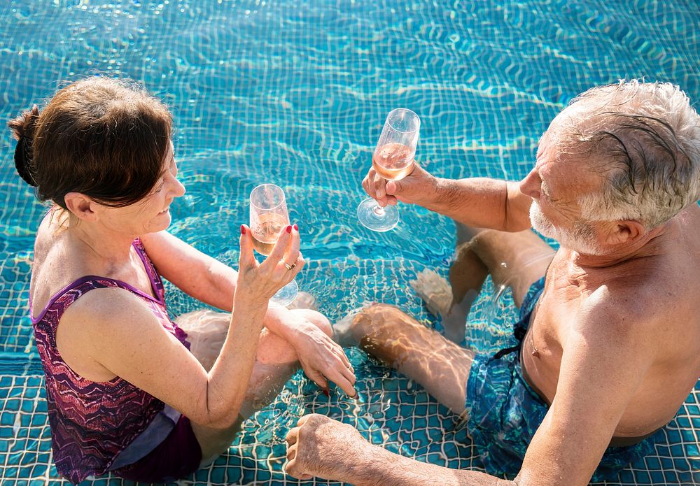 Senior couple drinking prosecco in a swimming pool