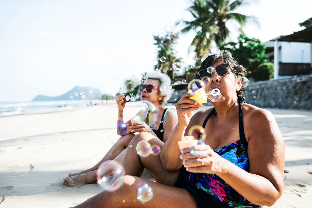 Senior friends blowing bubble and chilling on the beach