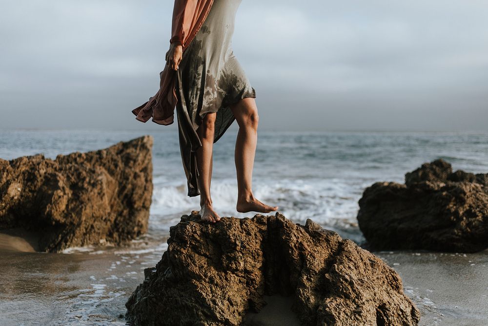 Woman's legs standing on a rock at the beach