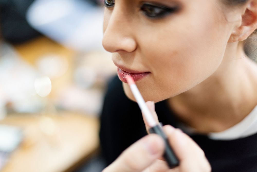 Makeup artist applying lip gloss onto model