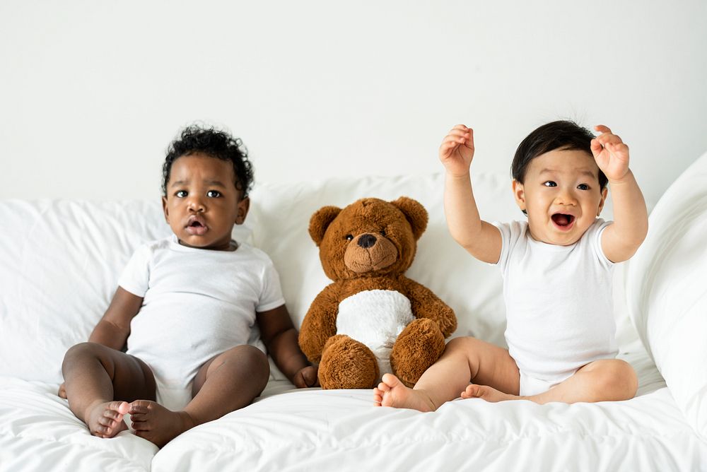 Babies and a teddy bear on the bed