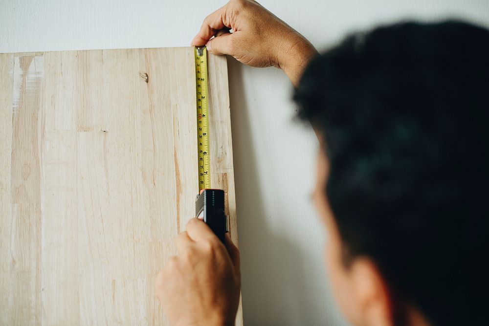 Man using a measuring tape on a wooden plank