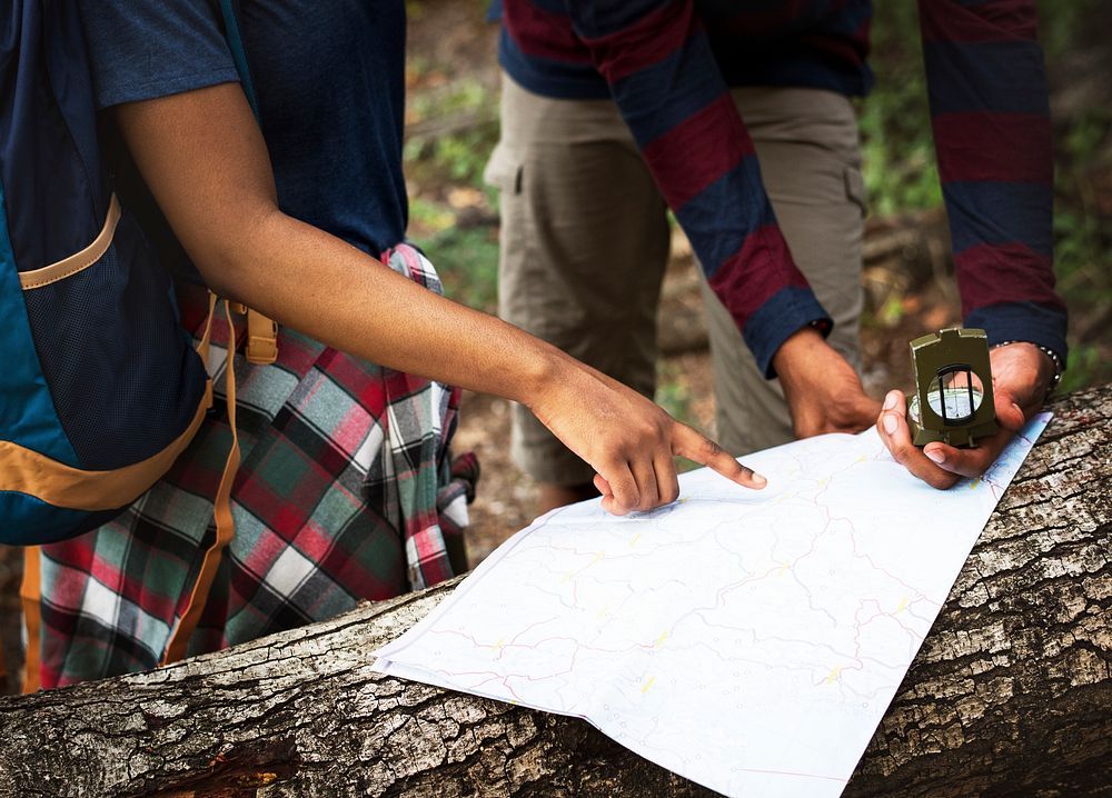 Trekking couple using map and compass in a forest