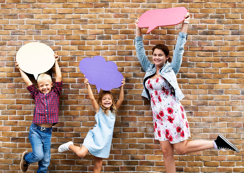 Kids showing blank colorful speech bubbles by a brick wall