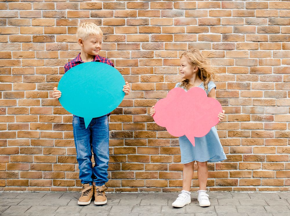 Kids holding blank speech bubbles by a brick wall