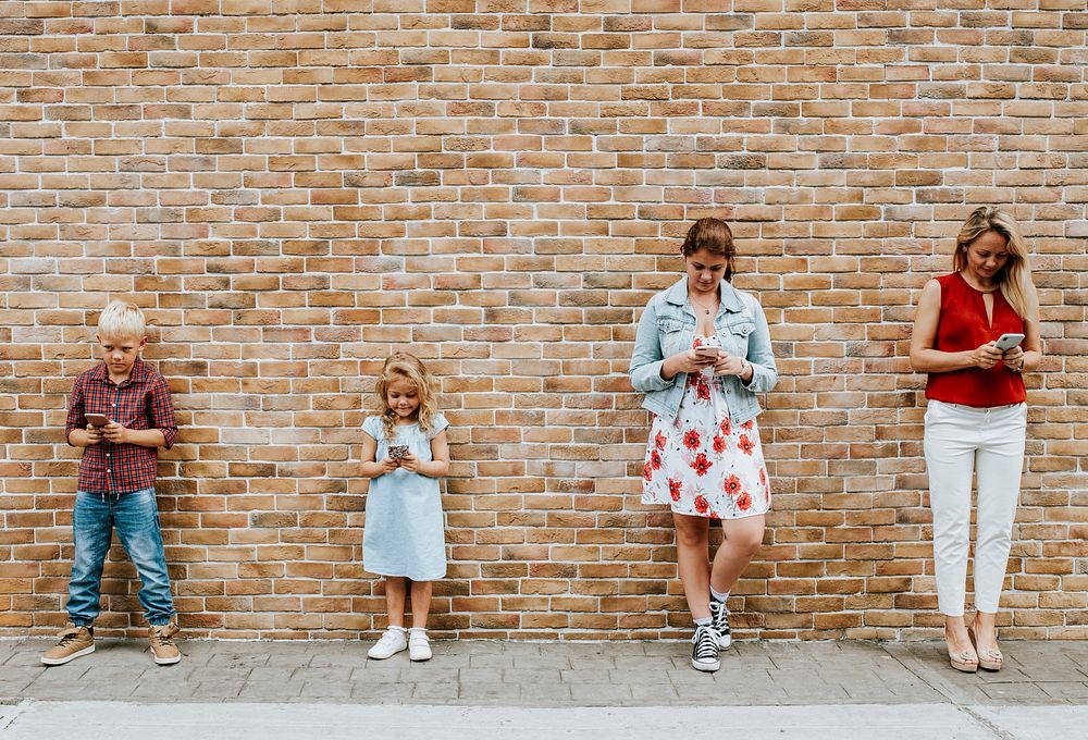 Mom and her kids texting by a brick wall