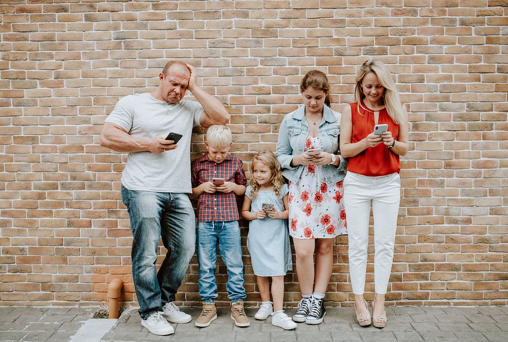 Phone addicted family standing by a brick wall