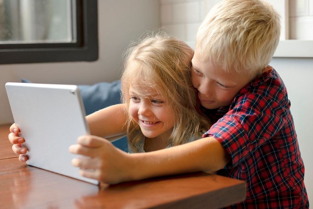 Little boy helping his sister to play a game on a digital tablet