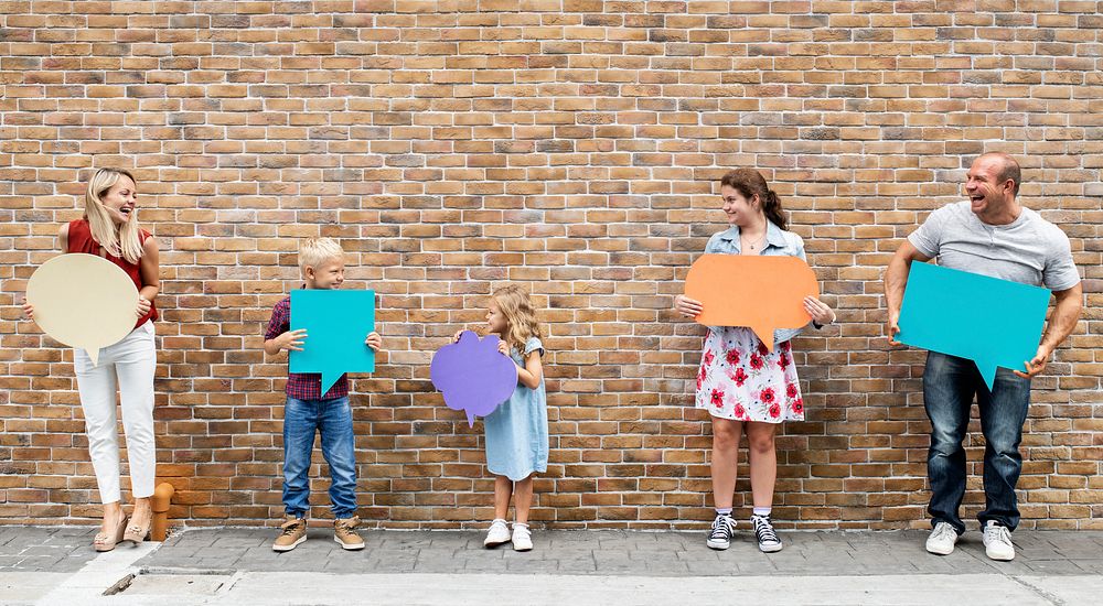 Family holding blank colorful speech bubbles by a brick wall