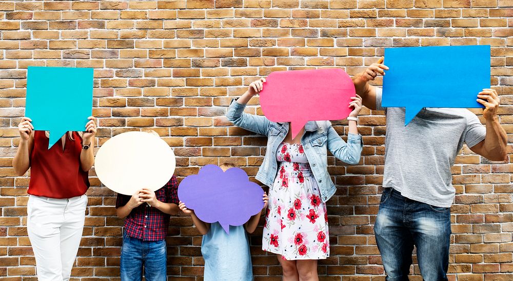 Family holding blank colorful speech bubbles by a brick wall
