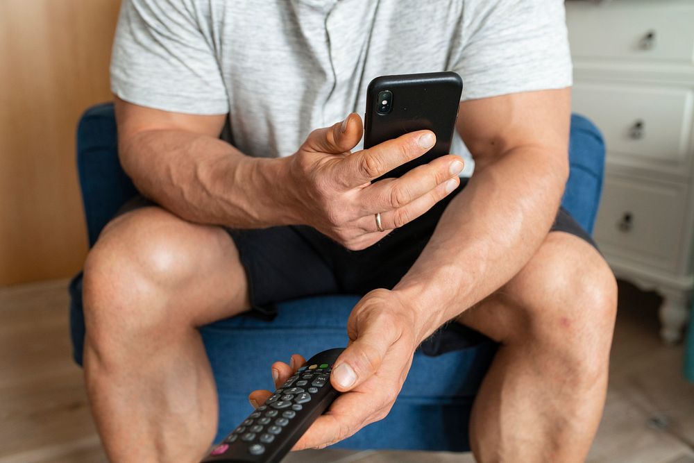 Man swapping between channels on the TV and on his phone
