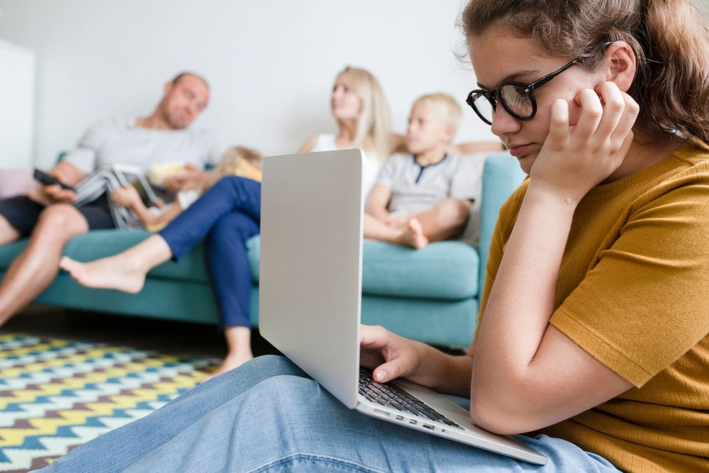 Young woman working on a laptop while her family is watching a movie