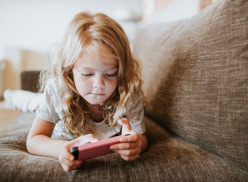 Little girl playing a mobile game on the couch