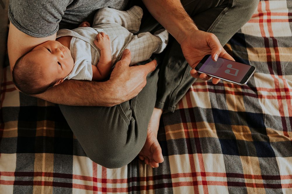 Father holding his baby while using his phone