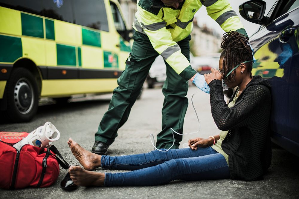 Male paramedic putting on an oxygen mask to an injured woman on a road