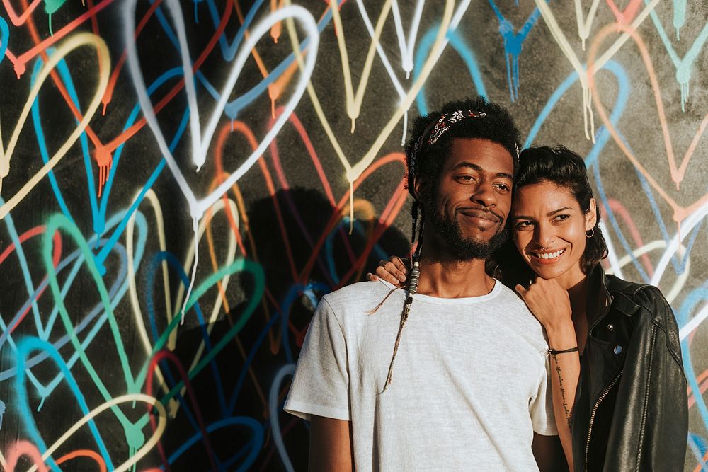 Happy couple posing for the camera against the backdrop featuring the graffiti artwork by James Goldcrown in Los Angeles…