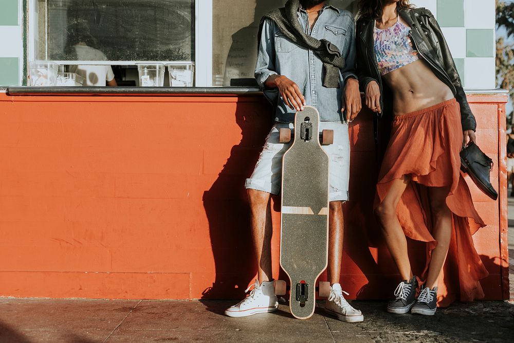 Young slim couple posing with a longboard