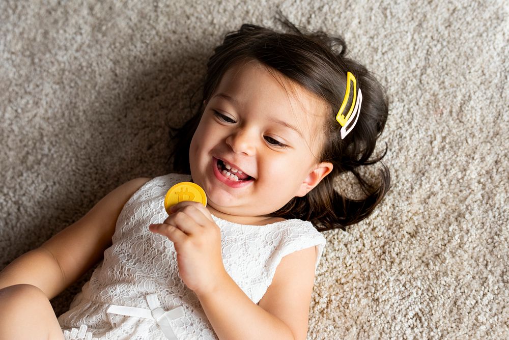 Smiling girl holding a bitcoin laying on carpet