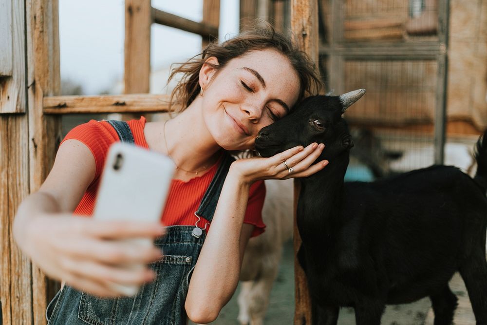 Happy girl taking a selfie with a black baby goat