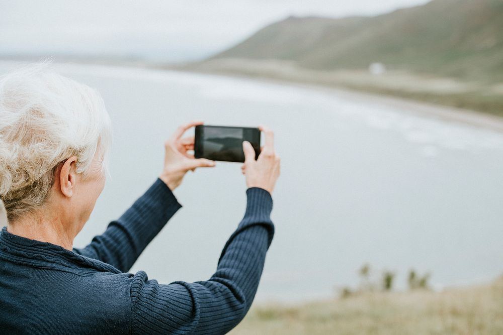 Elderly woman capturing a photo of the ocean
