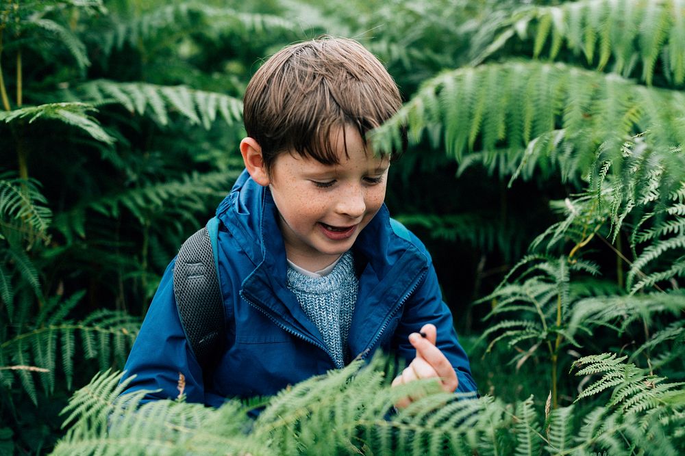 Happy kid standing near a fern tree