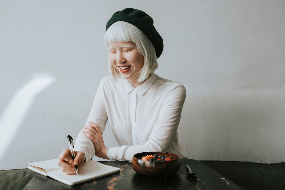 Cute albino woman writing in her journal at a cafe
